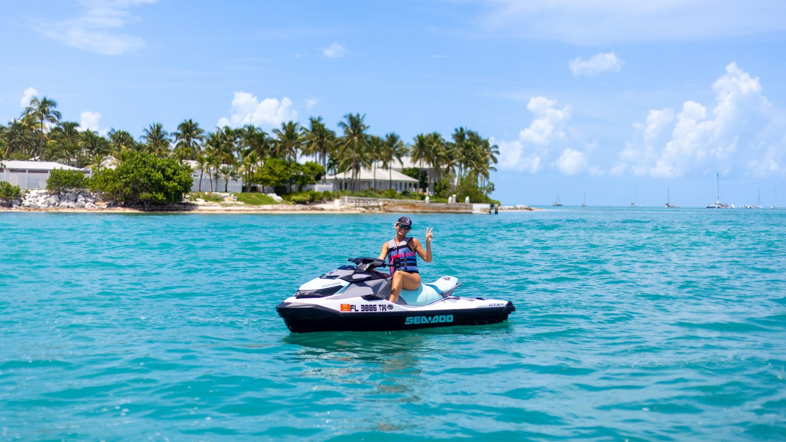 A rider on a white Sea-Doo idling on calm water with palm trees and waterfront houses on the Key West shoreline behind
