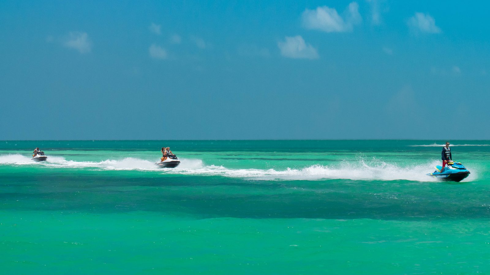A line of jet skis following the guide across flat turquoise water with mangrove islands on the horizon