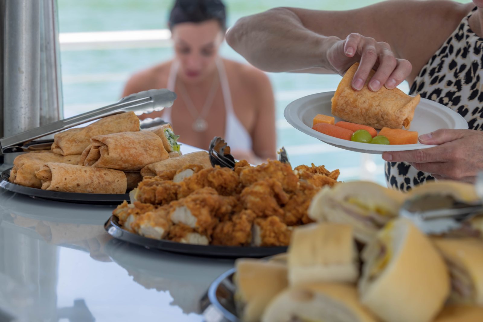 The lunch spread on board: trays of chicken tenders, wraps, Cuban sandwiches and fruit being served to guests