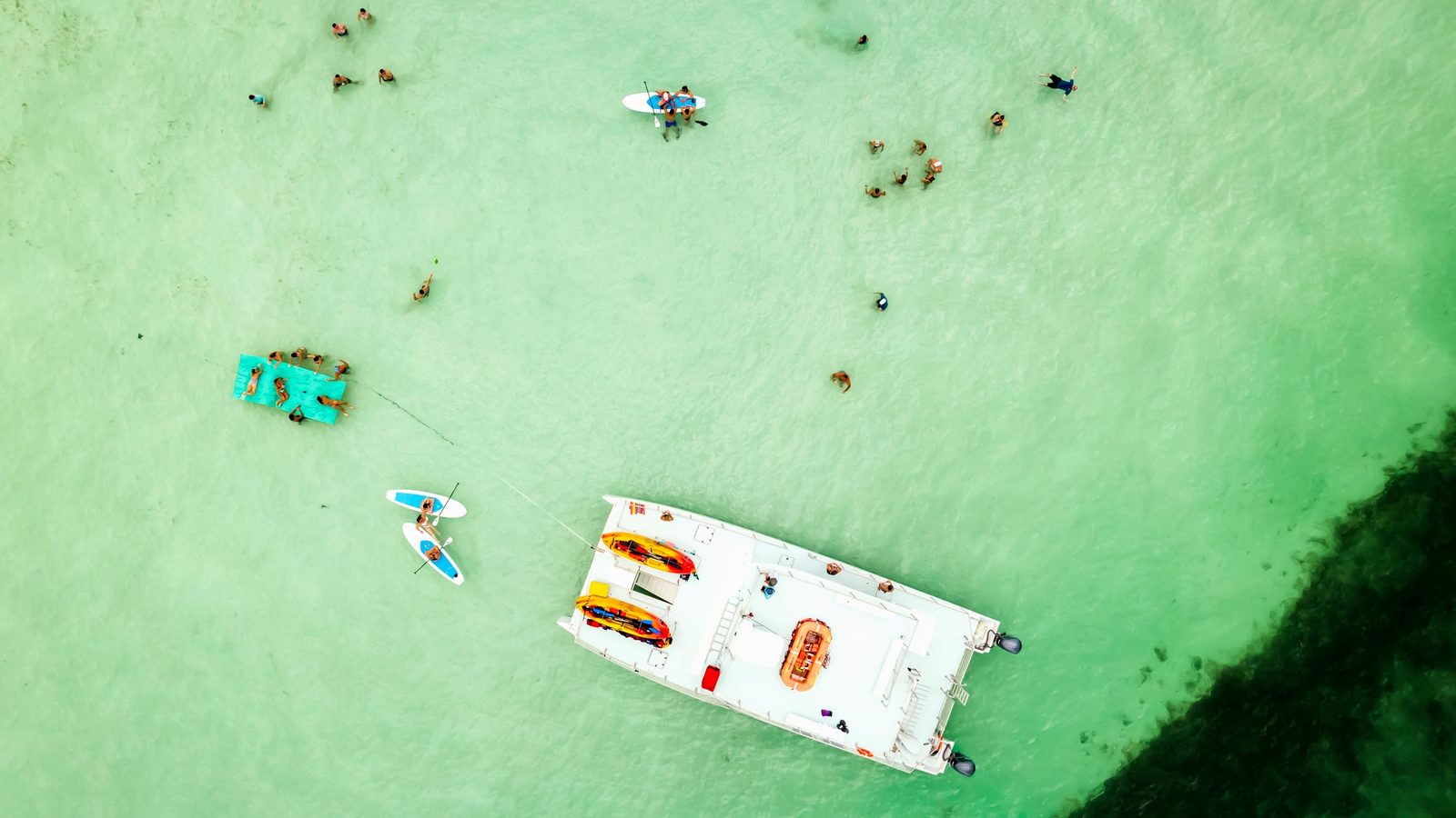 Aerial view of guests scattered across a shallow sandbar with kayaks, paddleboards and the catamaran anchored nearby