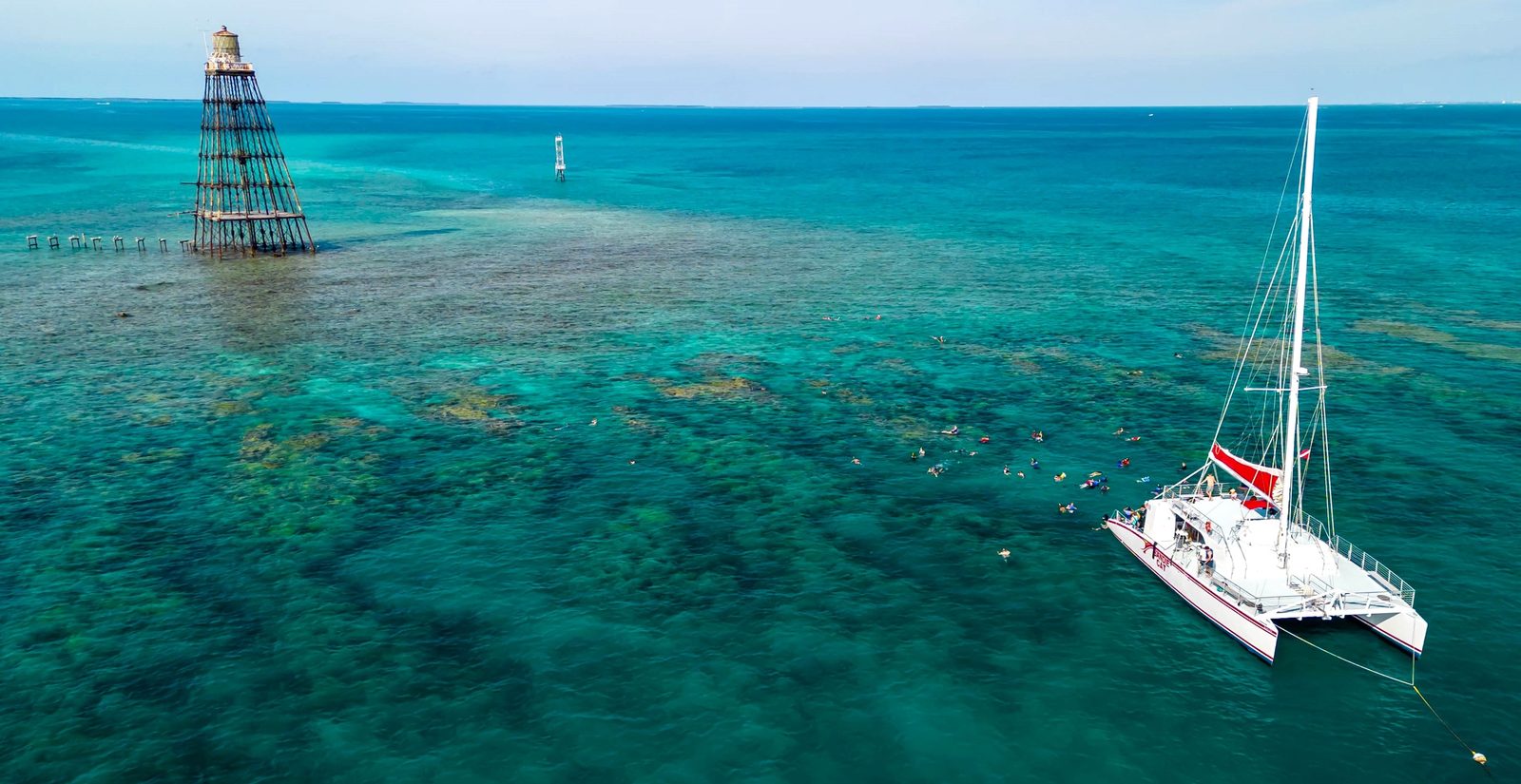 The Sandie Cat sailing catamaran anchored on the reef beside the Sand Key lighthouse tower in turquoise water