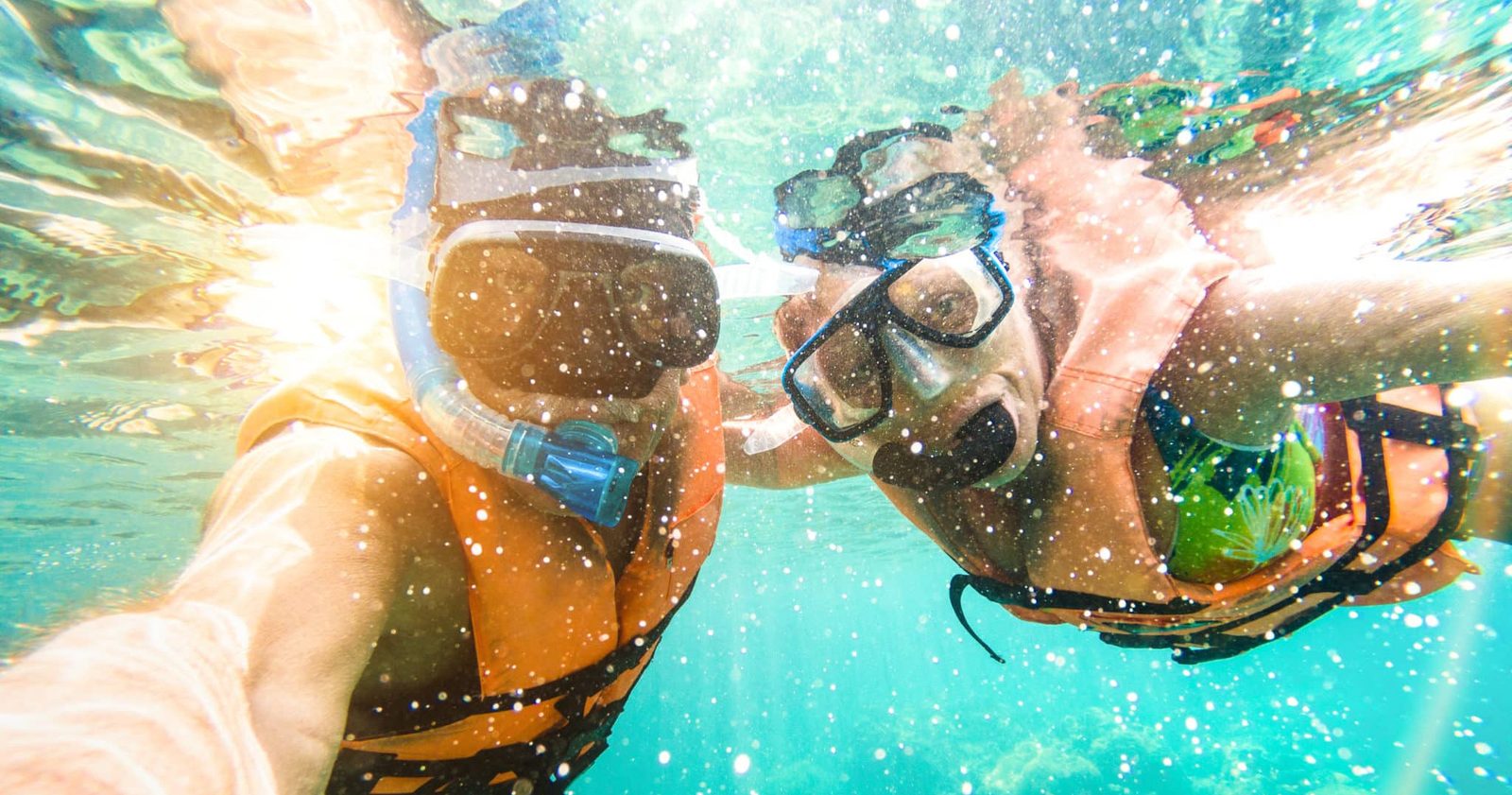 Two snorkelers in masks taking an underwater selfie with sunlight sparkling through the water