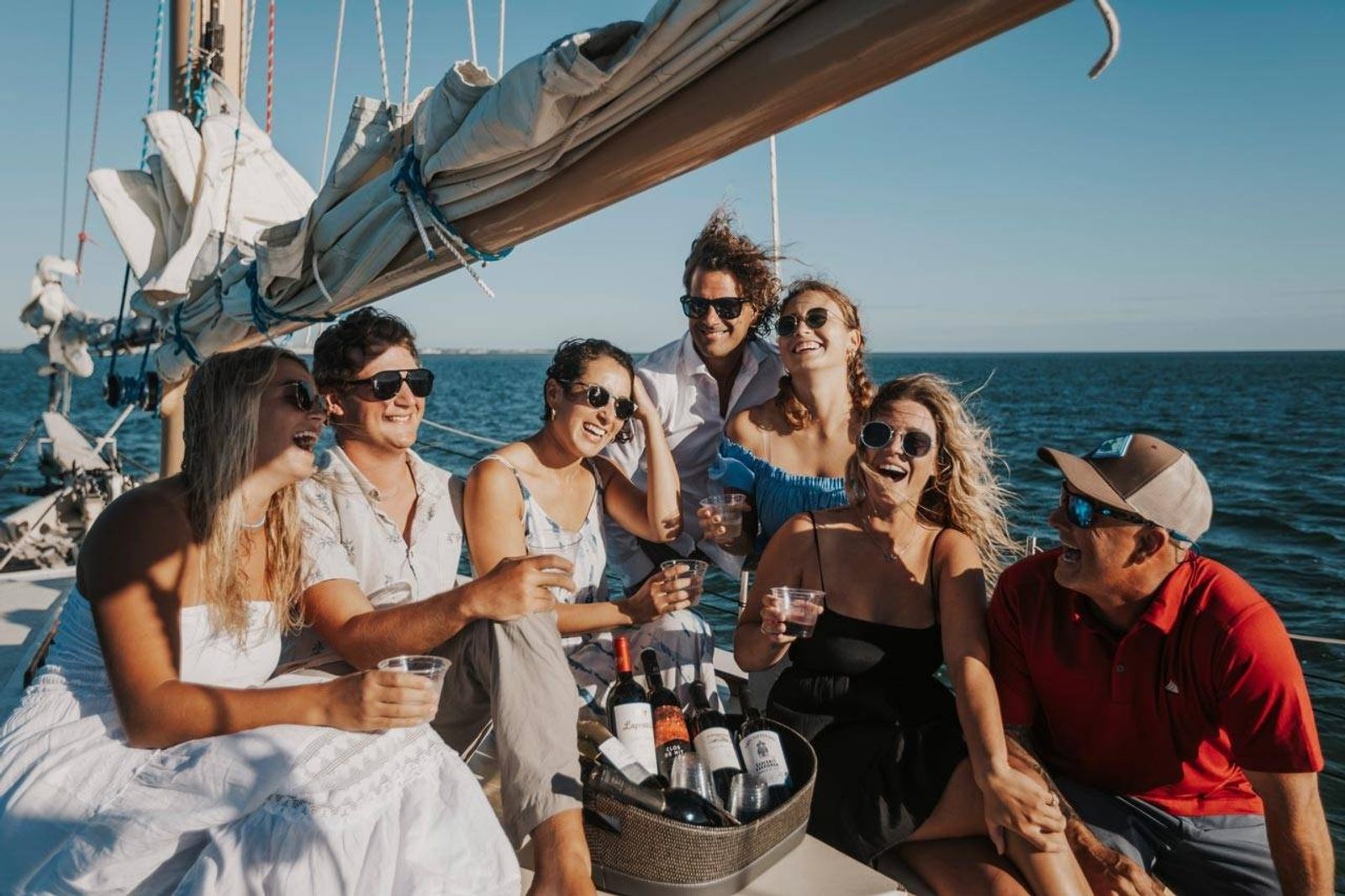 A group of friends raising wine glasses on the deck of a schooner under sail on a sunny afternoon