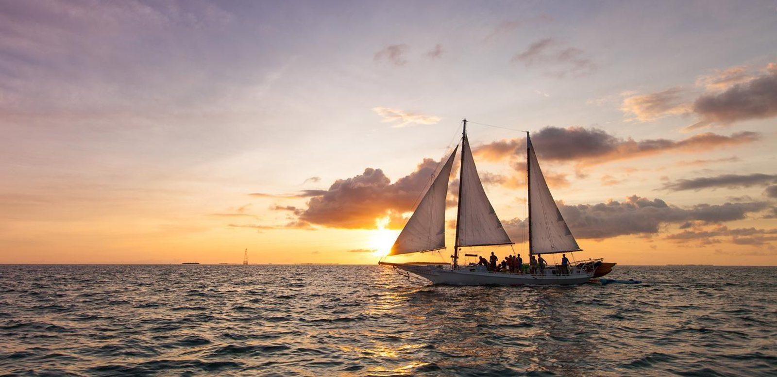 A two-masted schooner silhouetted against an orange and gray sunset sky off Key West
